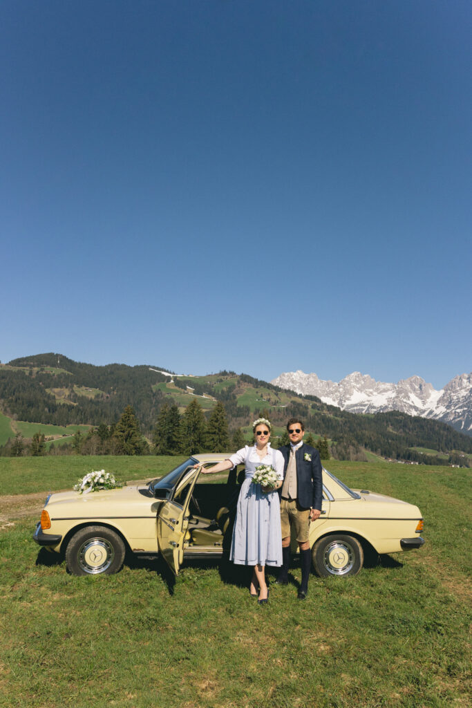 Braut mit Sonnenbrille und Blumenstrauß durch die Bergwiese – entspannte Hochzeit in den Kitzbüheler Alpen
