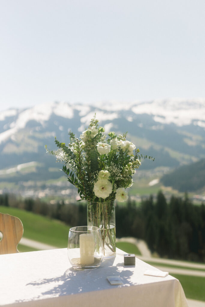 Hochzeitsstrauß auf dem Tisch mit Bergpanorama – florale Deko bei einer Alpenhochzeit in Kitzbühel